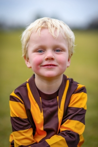 Little boy in Aussie Rules Football uniform on field with ball - Australian Stock Image