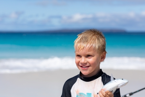 little boy on beach holding small fish he has caught - Australian Stock Image