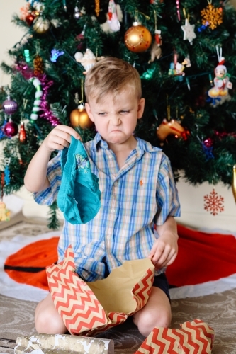 Little boy pulling a face, unhappy with a gift of underpants he has received on Christmas day - Australian Stock Image