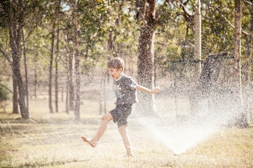 Little boy running under sprinkler in backyard in summer - Australian Stock Image