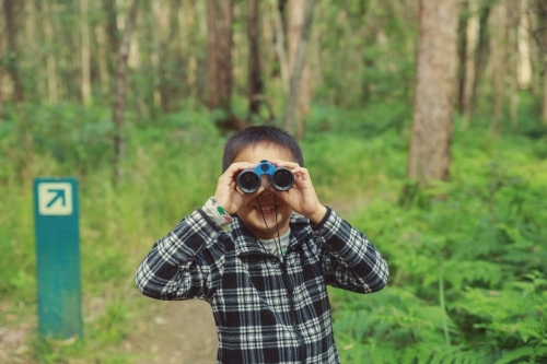 Little boy using binoculars in the forest - Australian Stock Image