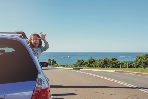 Little girl in the car on roadside with ocean background