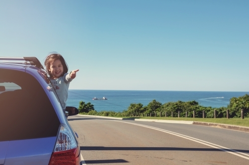 Little girl in the car on roadside with ocean background - Australian Stock Image