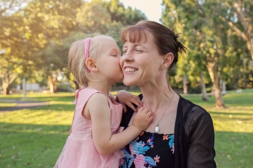Little girl kissing her mother in the park - Australian Stock Image