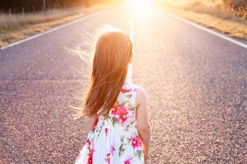 Little girl looking towards sunset along road - Australian Stock Image