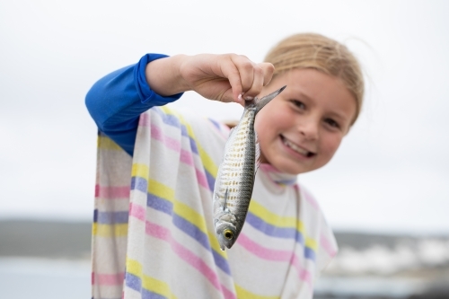 little girl on the beach holding up a little fish she caught - Australian Stock Image