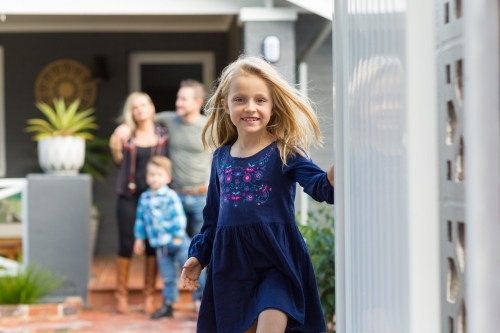 Little girl opening front gate in front of family home