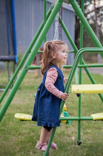 Little girl playing on a swing set and slide in the backyard - Australian Stock Image