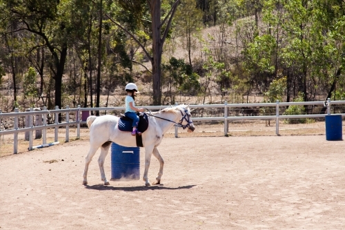 Little girl riding a white pony in dusty yard at riding school - Australian Stock Image