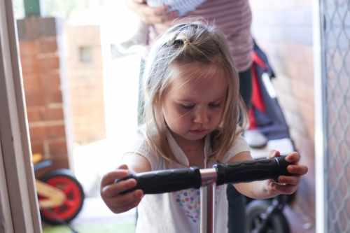 Little girl riding through a doorway on her scooter. - Australian Stock Image