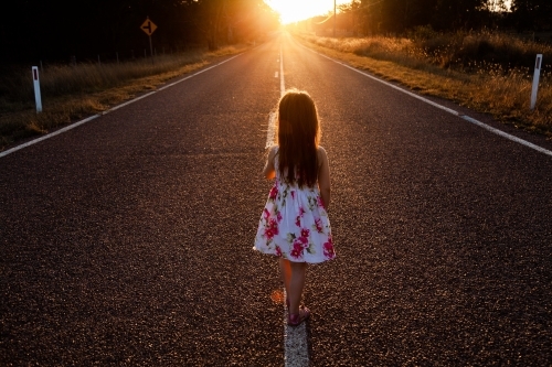Little girl walking along the road towards the sunset light - Australian Stock Image