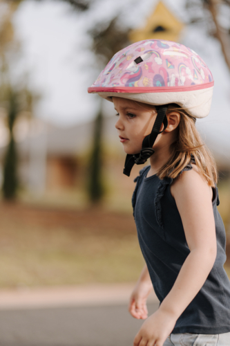 Little girl wearing pink helmet playing outside - Australian Stock Image