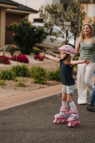 Little girl wearing pink helmet while on roller skates spreads her arms wide open. - Australian Stock Image