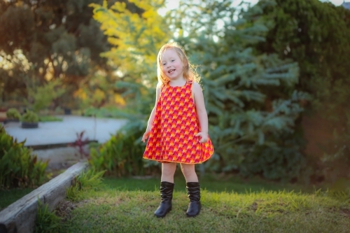 Little girl wearing red dress exploring lush green garden - Australian Stock Image