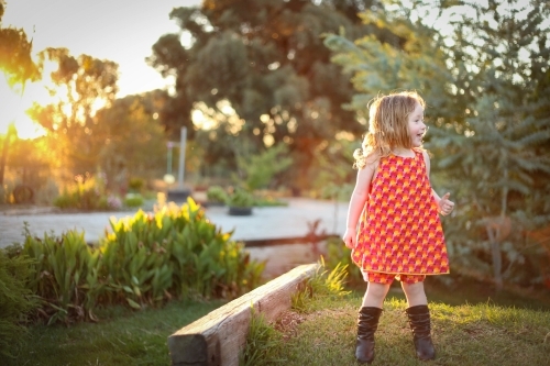 Little girl wearing red dress exploring lush green garden - Australian Stock Image