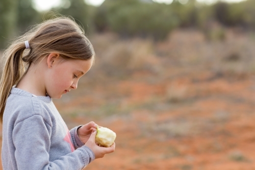 Little girl with apple outside with red dirt - Australian Stock Image