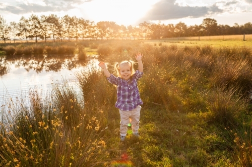 Little girl with arms up saying yay in golden light on farm celebrating after rain - Australian Stock Image