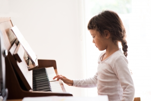 Little girl with Asian ethnicity learning to play the piano. - Australian Stock Image