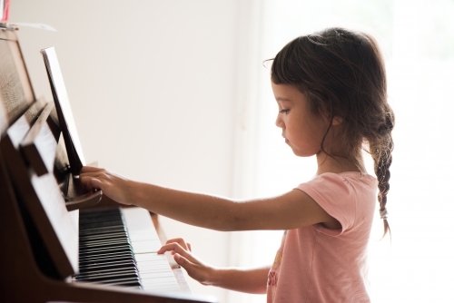 Little girl with Asian ethnicity learning to play the piano. - Australian Stock Image