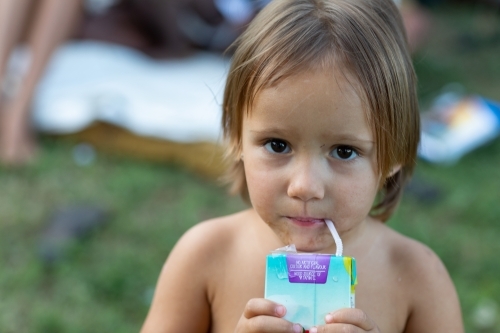little girl with grubby face drinking from juice box - Australian Stock Image