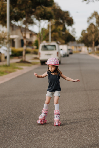 Little girl with pink helmet and four-wheeled roller skates on the street - Australian Stock Image