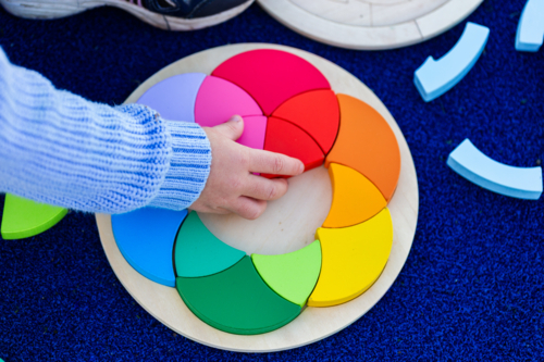Little girls hands doing colourful puzzle game at preschool - Australian Stock Image