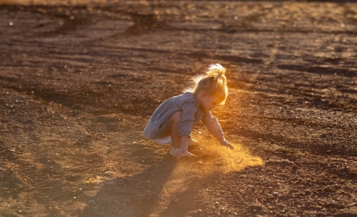 little kid playing in the dirt with backlight highlighting dust - Australian Stock Image