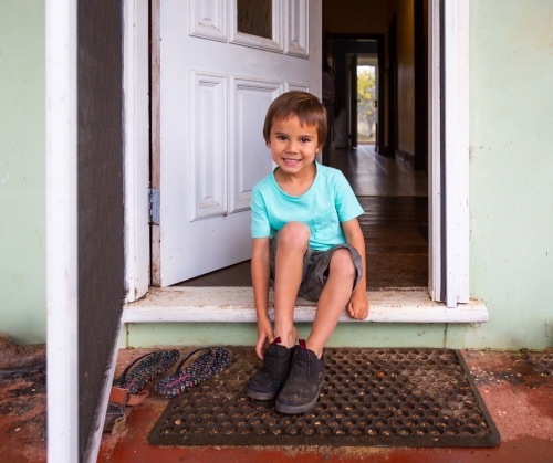 Little kid sitting on doorstep putting on shoes - Australian Stock Image