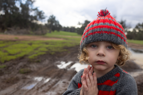 little kid wearing knitted beanie and jumper outdoors on a farm in winter - Australian Stock Image