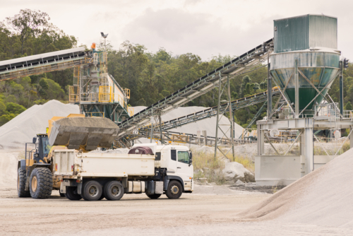 Loader and tipper truck at a quarry site with machinery in background - Australian Stock Image