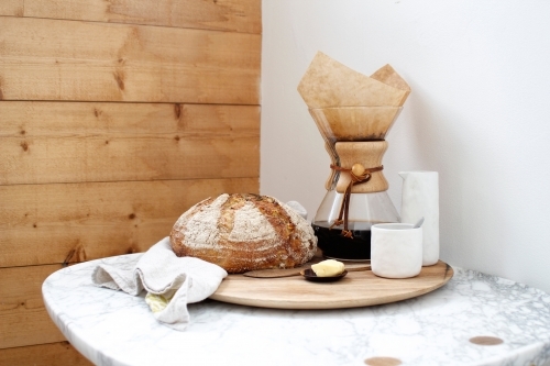 Loaf of bread and butter with filter coffee on wooden board on marble table