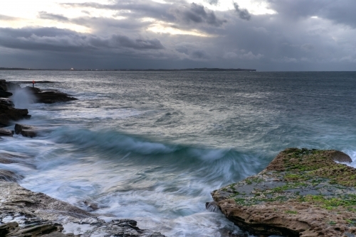 Lone person fishing on rock at moody sunrise - Australian Stock Image