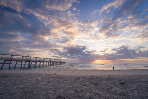 Lone person walking on beach at sunrise - Australian Stock Image