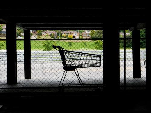 Lone shopping trolley in dark supermarket parking area - Australian Stock Image