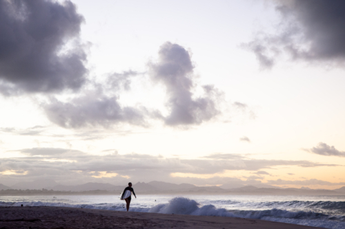Lone surfer walking along beach at dusk - Australian Stock Image
