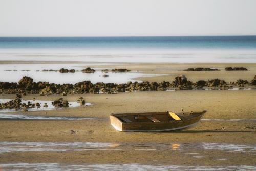 Lone wooden boat sitting on sand at low tide - Australian Stock Image