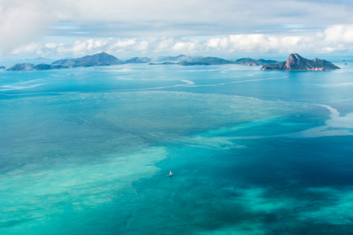 Lonely yacht drifting over turquoise reef waters - Australian Stock Image