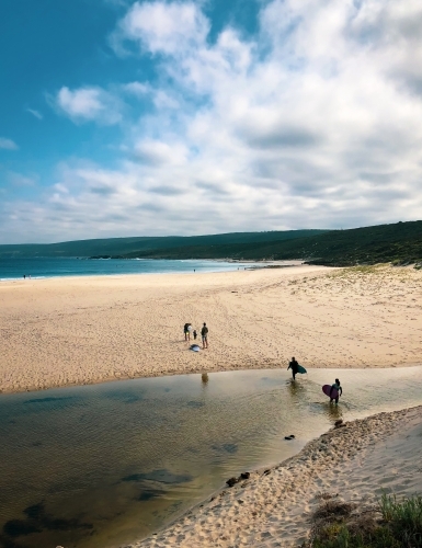 Long coastal shot of people carrying surfboards over river crossing  to remote location - Australian Stock Image