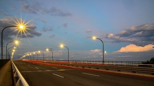 Long exposure of cars driving over a bridge at dusk with the rising moon in the background - Australian Stock Image