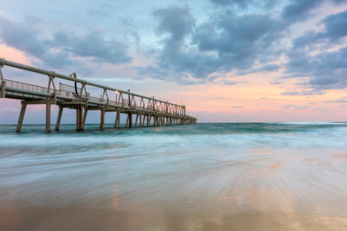 Long jetty stretching into the ocean with a pastel, cloudy sky - Australian Stock Image