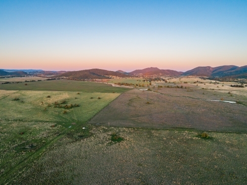 Long shadowed landscape and dusk light on distant hills over pastoral land - Australian Stock Image