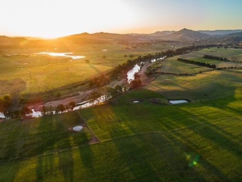 Long shadows cast over farmland from trees beside hunter river at sunset - Australian Stock Image