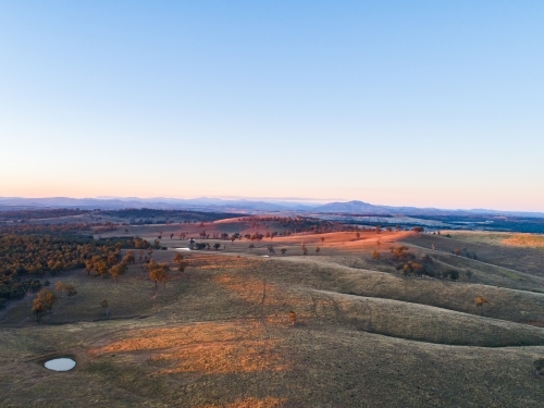 Long shadows on hills in paddock with small dam - Australian Stock Image