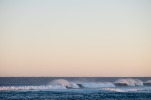 Long shot of breaking waves with spray and pastel sky - Australian Stock Image