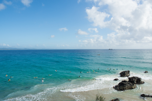 Long shot of surfers in water waiting for a wave in the sunshine - Australian Stock Image