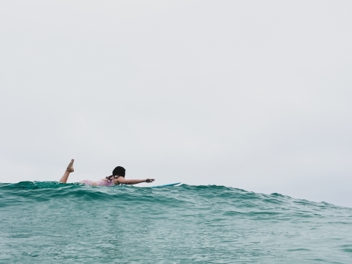 Long shot of Woman in bathers on surfboard paddling on ocean for surf - Australian Stock Image