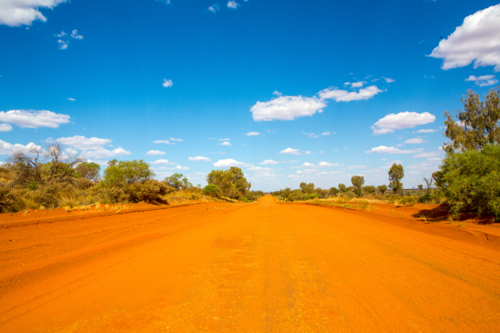Long unsealed burnt-orange track in an outback - Australian Stock Image
