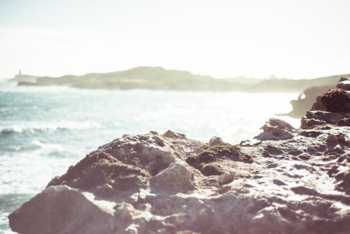 Looking across rocky coastline over bay on sun haze - Australian Stock Image
