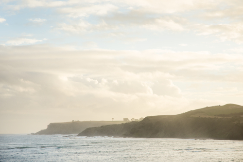 Looking across the ocean to cliffs in misty, golden, late afternoon light - Australian Stock Image
