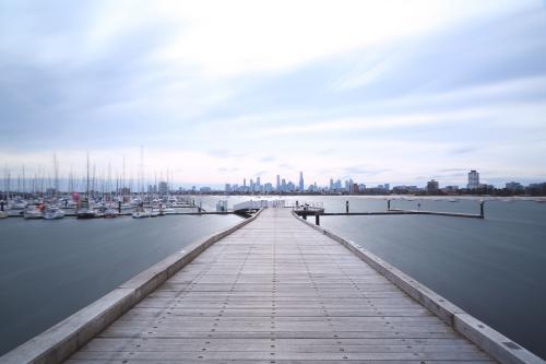 Looking along jetty to moored boats and city in distance - Australian Stock Image